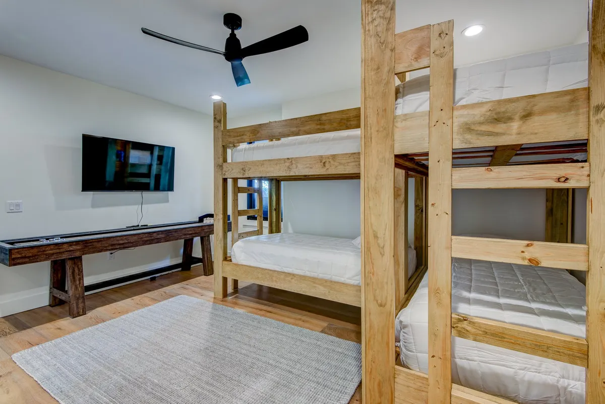 A playful, inviting bunk suite is pictured with two twin-over-twin bunk beds, a sturdy wooden table, and a television. The cozy arrangement is designed for shared laughter and fun, ideal for children or groups of friends. Decorative touches and a relaxed mood make this suite both practical and whimsical.