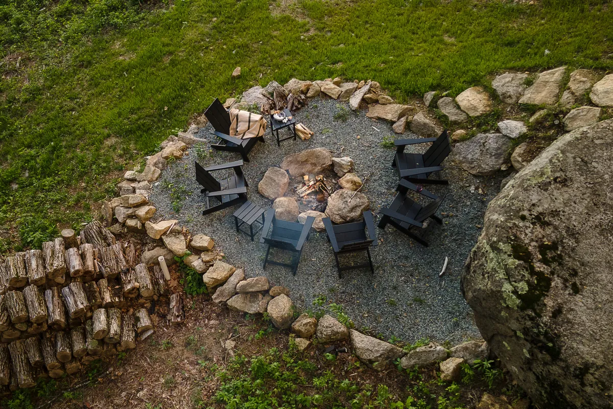 A communal outdoor fire pit area surrounded by comfortable chairs and dramatic rock formations. The fire glows invitingly, suggesting evenings of storytelling, laughter, and marshmallow roasting under the stars.