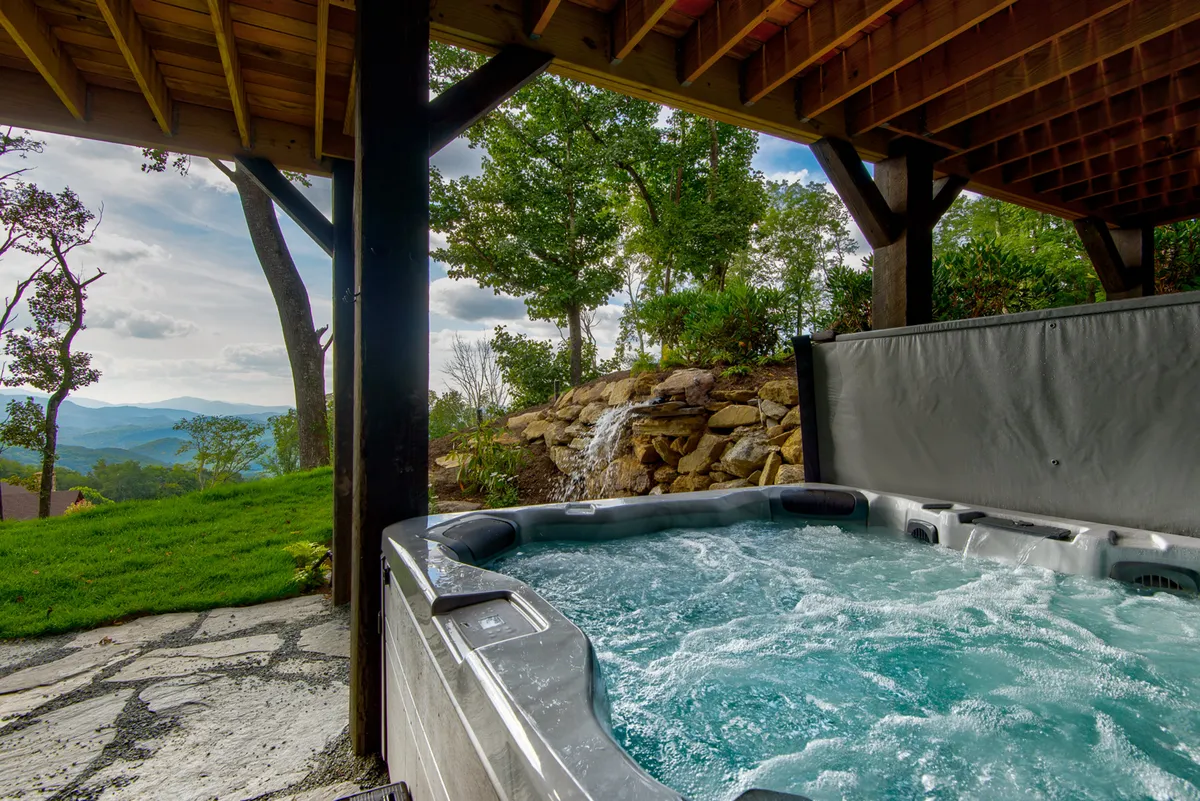 A tranquil outdoor patio featuring a hot tub with a built-in waterfall, all set against a stunning mountain backdrop. The space invites relaxation and socializing, especially at sunset.