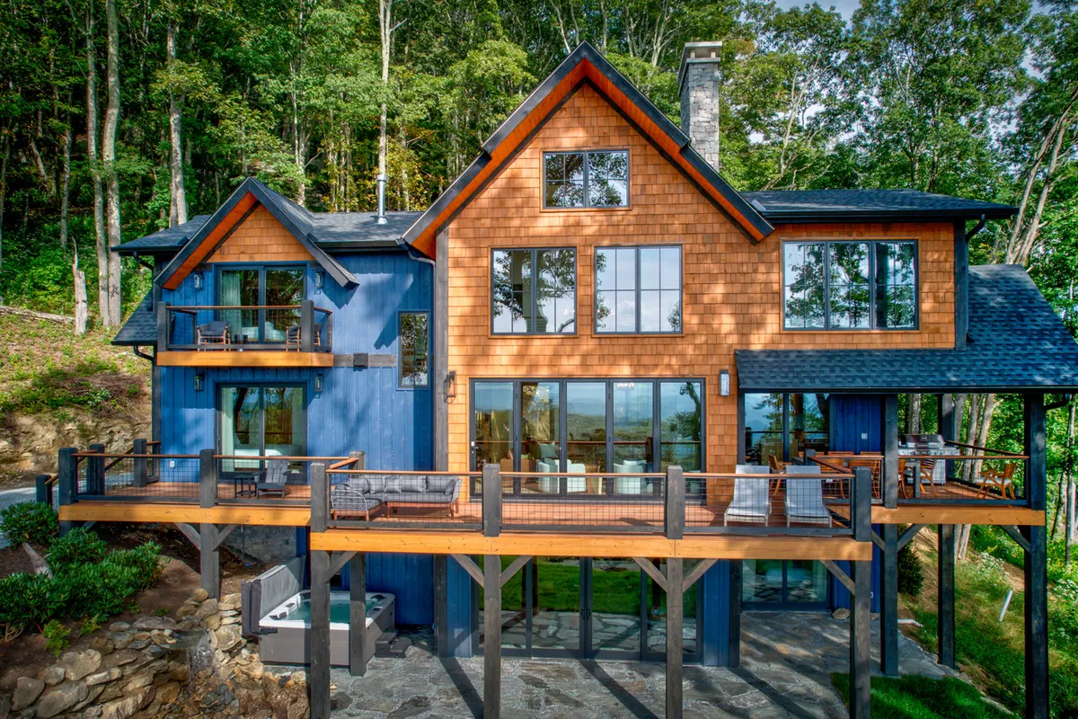 A tranquil exterior scene featuring a wooden deck, large windows, and surrounding trees, with hints of both relaxation and activity. The deck invites guests to enjoy nature, whether sipping morning coffee, dining outdoors, or stargazing, framed by the comfort of the mountain home.
