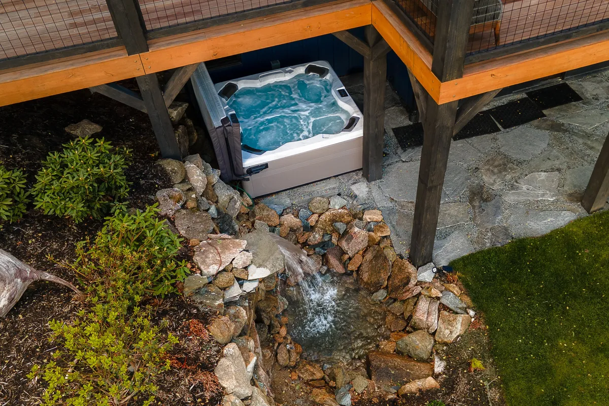 A tranquil hot tub set against lush landscaping and a gentle waterfall, suggesting relaxation after a day of outdoor activity. The scene is peaceful, with the promise of winding down while immersed in nature.